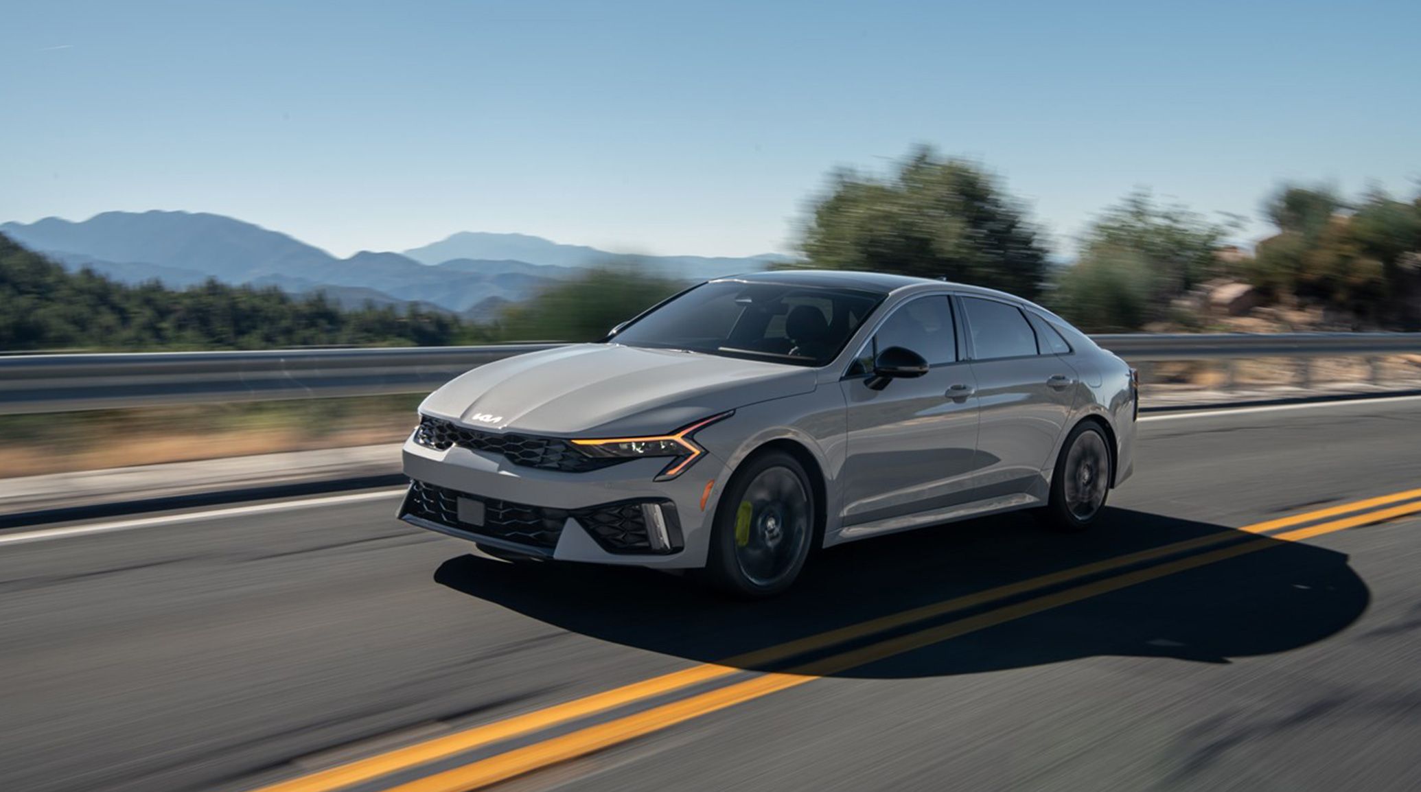 The 2025 Kia K5 sedan looking stylish and sleek driving on a mountain road.